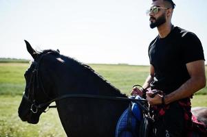 Arab tall beard man wear in black and sunglasses ride arabian horse. photo