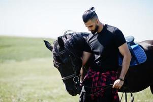 Hombre árabe de barba alta vestido de negro con caballo árabe. foto