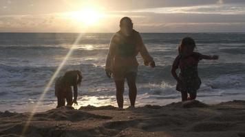 felice famiglia asiatica di madre e figlie divertendosi a giocare sulla spiaggia durante le vacanze estive al tramonto. gita estiva in famiglia al mare. concetto di viaggio e vacanza. video