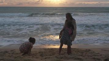 felice famiglia asiatica di madre e figlie divertendosi a giocare sulla spiaggia durante le vacanze estive al tramonto. gita estiva in famiglia al mare. concetto di viaggio e vacanza. video