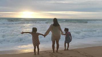 gelukkige Aziatische familie van moeder en dochters die plezier hebben met spelen op het strand tijdens de zomervakantie bij zonsondergang. zomer familie-uitstapje naar het strand. reis- en vakantieconcept. video