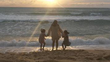 felice famiglia asiatica di madre e figlie divertendosi a giocare sulla spiaggia durante le vacanze estive al tramonto. gita estiva in famiglia al mare. concetto di viaggio e vacanza. video