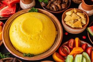 comida rumana casera con polenta, carne, queso y verduras. deliciosas gachas de maíz en platos de barro. mamaliga o polenta, un plato tradicional en moldavia, hungría y cocina ucraniana. foto