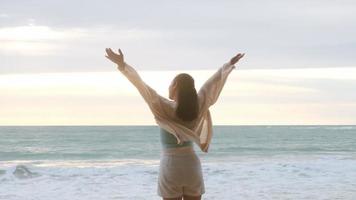 ritratto di una bella donna asiatica sorridente rilassante sulla spiaggia. una giovane donna che passeggia lungo il mare guardando le grandi onde e i forti venti. concetto di relax e viaggi in vacanza. video