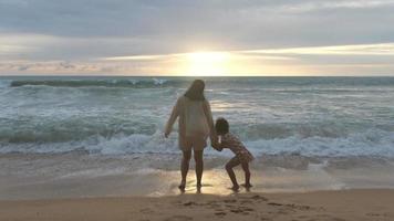 felice famiglia asiatica di madre e figlia divertendosi a giocare sulla spiaggia durante le vacanze estive al tramonto. gita estiva in famiglia al mare. concetto di viaggio e vacanza. video