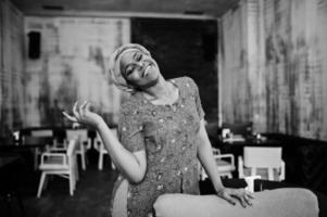 Stylish african woman in red shirt and hat posed indoor cafe. photo