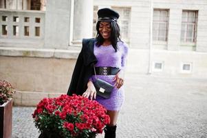 African american woman at violet dress and cap posed outdoor. photo