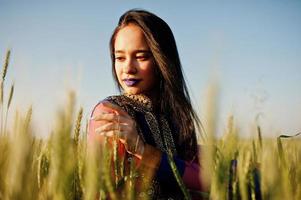 Tender indian girl in saree, with violet lips make up posed at field in sunset. Fashionable india model. photo