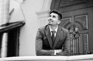 Elegant indian fashionable man model on suit posed at winter day leaned on the railing. photo