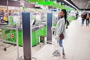mujer africana posada en suéter y jeans posada en el supermercado contra el cajero. foto