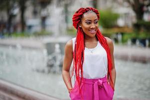 Fashionable african american girl at pink pants and red dreads posed outdoor against fountains. photo