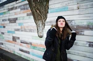 una joven usa sombreros negros contra una pared de madera. foto