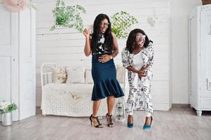 Two african woman friends wear on eyeglasses posed indoor white room. Laughing and having fun together. photo