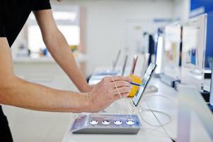 Seller man mobile phone professional consultant in tech store or shop hold new smartphone at hand and use stylus. photo