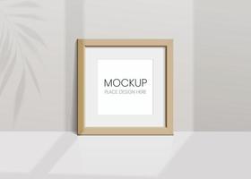 Realistic vector mockup with wooden photo frame. Shadow on the wall and empty place for your design. 3d soft light and overlay shadow from leaves of plant and window. Square poster or painting.