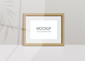 Realistic vector mockup with wooden photo frame. Shadow on the wall and empty place for your design. 3d soft light and overlay shadow from leaves of plant and window. Horizontal poster or painting.