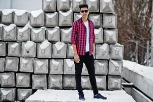 Un joven indio casual con camisa a cuadros y gafas de sol posó contra bloques de piedra. foto