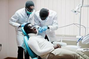paciente afroamericano en silla dental. oficina de dentista y concepto de práctica médica. dentista profesional ayudando a su paciente en odontología médica. taladrar los dientes del paciente en la clínica.