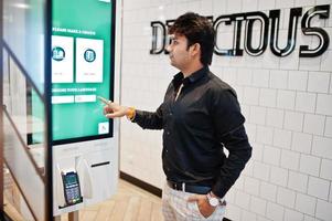 Indian man customer at store place orders and pay through self pay floor kiosk for fast food, payment terminal. Make a choise of language on screen. photo