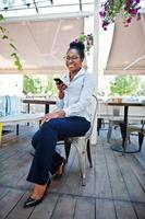 African american girl wear in glasses with mobile phone sitting at outdoor caffe. photo