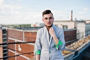 Dreamer stylish macho man in gray suit and glasses posed on the roof. photo