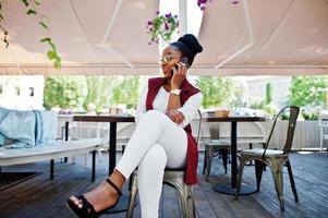 African american girl wear in glasses with mobile phone sitting at outdoor caffe. photo