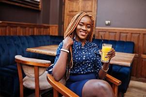 Portrait of beautiful young african business woman, wear on blue blouse and skirt, sitting with juice in cafe. photo