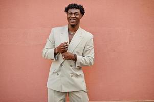 Stylish afro man in beige old school suit against pink wall. Fashionable young African male in casual jacket on bare torso. photo