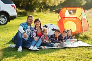 Family spending time together. Four kids and parents outdoor in picnic blanket. Large family in checkered shirts. photo