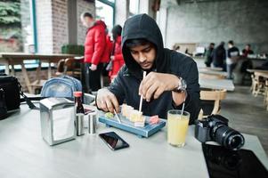 Casual and stylish young asian man on hood at cafe eating sushi. photo