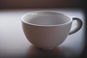 An old white teacup was placed on the table in the morning with light and shadow. photo