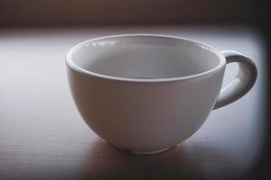 An old white teacup was placed on the table in the morning with light and shadow. photo