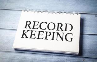 RECORD KEEPING word on notepad and blue wooden background photo