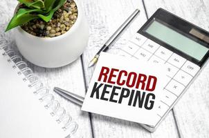 Text RECORD KEEPING on paper card and calculator on wooden background photo
