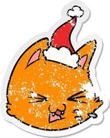 spitting distressed sticker cartoon of a cat face wearing santa hat vector