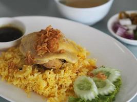 Chicken Biryani food, yellow color Traditional Indian dish of rice and chicken marinated in spices with green sauce, white plate on table photo