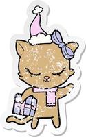 cute distressed sticker cartoon of a cat with present wearing santa hat vector