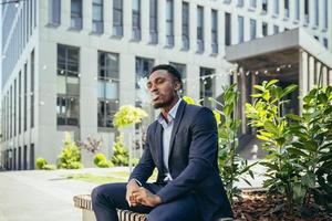 african american business man smoking cannabis outdoors sitting on city park bench photo