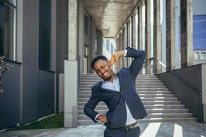 Businessman has severe back pain at work, african american freelancer man near office photo