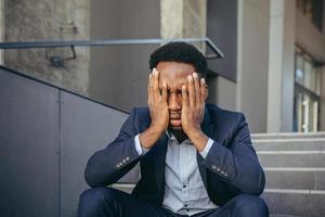 hombre de negocios africano sentado frustrado en las escaleras deprimido por los resultados de su trabajo foto