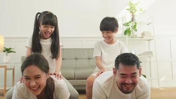 Happy well-being Asian Thai family, children play and tease their parents while yoga fitness training and health exercise together in the white living room, domestic home lifestyle, weekend activity. video