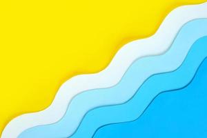 Seashore diagonal background made of color paper. Yellow beach sand with copy space and paper cut blue waves. Summer sea holidays concept. Relaxation and fun on vacations. The ocean coast layout. photo