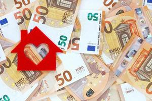 Red felt small house on 50 fifty euro banknotes background. Heart-shaped hole is cut instead of a window. Real estate loan concept. Money for a dream house. Place for text. photo