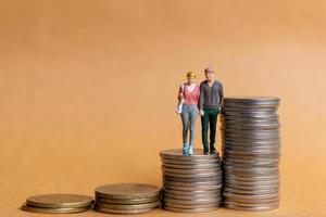 gente en miniatura, pareja feliz de pie en la pila de monedas foto