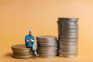 Miniature people, Businessman sitting on coins stack photo