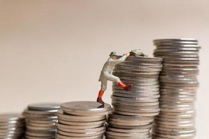 Miniature people Mountain climber ascending the coin stack photo