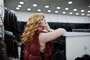 Elegance blonde girl in fur coat at the store of fur coats and leather jackets. photo