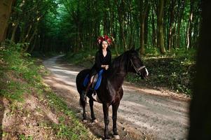 Mystical girl in wreath wear in black at horse in wood. photo