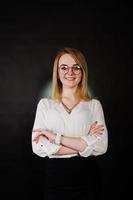 Studio portrait of blonde businesswoman in glasses, white blouse and black skirt against dark background. Successful woman and stylish girl concept. photo