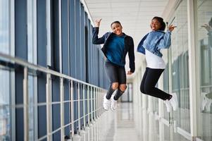 Two african woman friends in jeans jacket jumps indoor together. photo